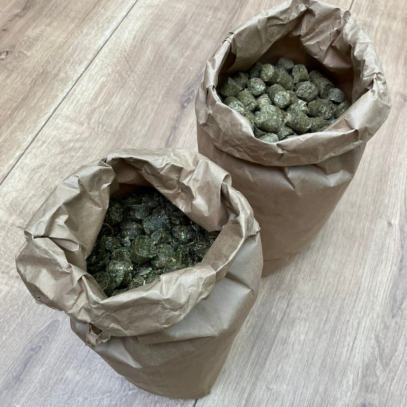 Zwei geöffnete Papiersäcke mit HEUFEIN Heucobs stehen nebeneinander auf dem Hallenboden — das 5-kg- und das 25-kg-Gebinde.